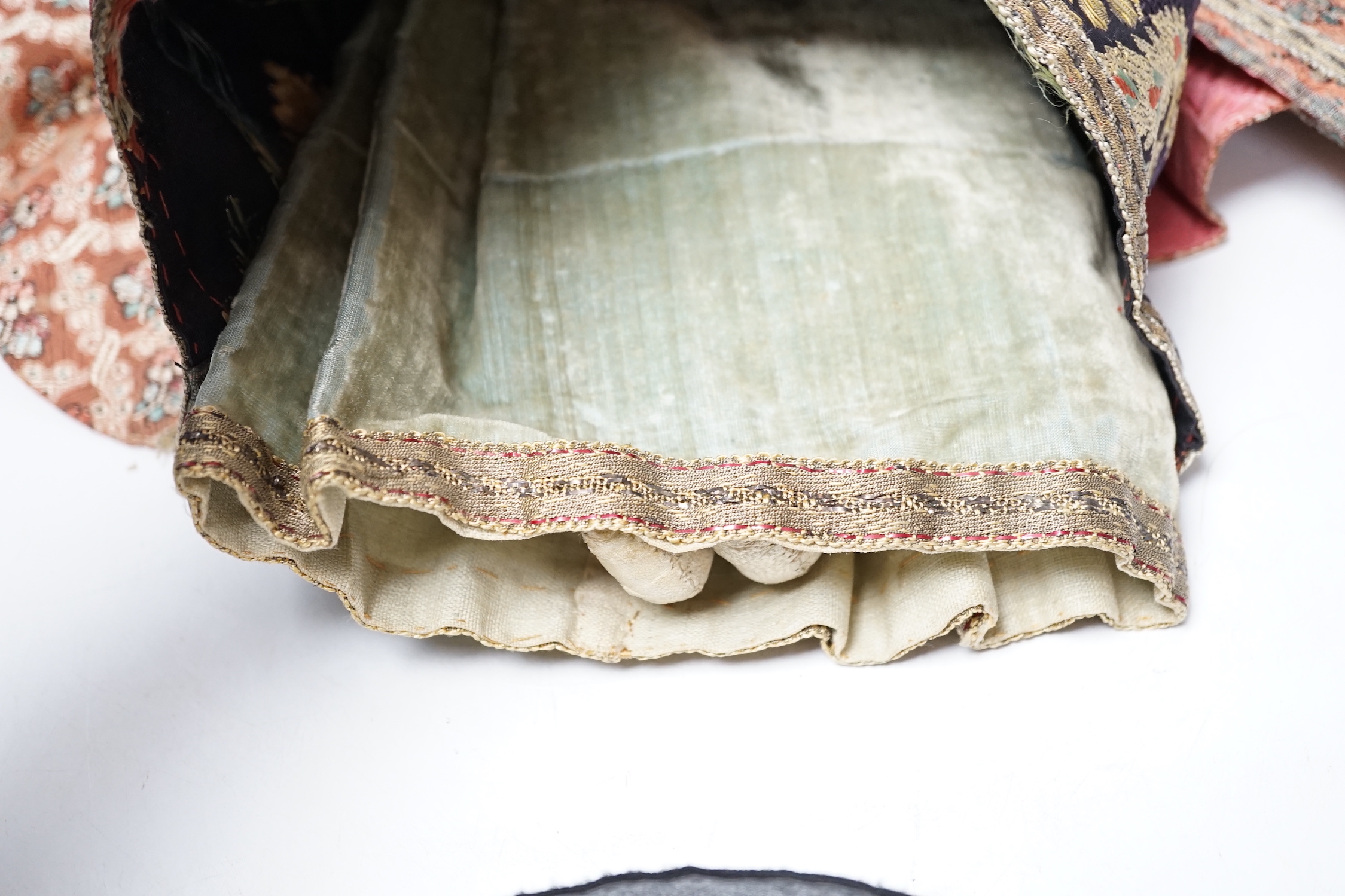 An early 19th century doll with a papier mache head, glass eyes and kid leather body, dressed in 18th century embroidered brocade and silk costume, possibly religious, 40cm high